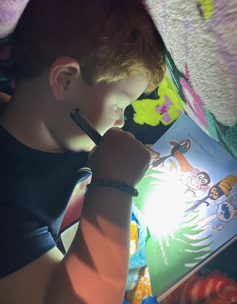Boy reading with flashlight under blanket to complete reading challenge