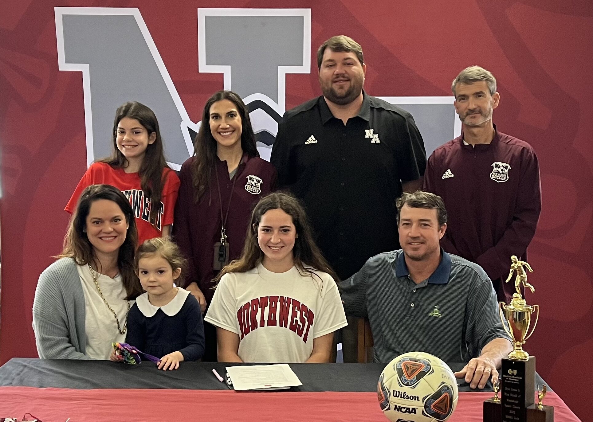 New Albany Lady Bulldog Soccer Player Caroline King (front center) is surrounded by family and coaches as she signs to play soccer for Northwest Mississippi Community College on Thursday, February 17. Pictured front row l-r:  Bailey King, Elizabeth King, Caroline King, Geoffrey KingBack row l-r:  Sara Jane King; Katelyn Robbins, NAHS Assistant Soccer Coach; Cody Stubblefield, NAHS Athletic Director; Bert Anderson, NAHS Head Girls Soccer Coach.